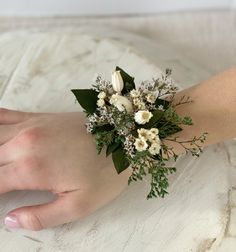 a woman's hand holding a bouquet of flowers on top of a white surface