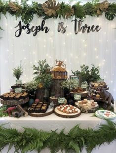 a table topped with lots of desserts and greenery next to a sign that says joseph is three