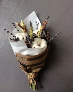 a bouquet of dried lavenders and cotton in a paper wrapped vase on a table