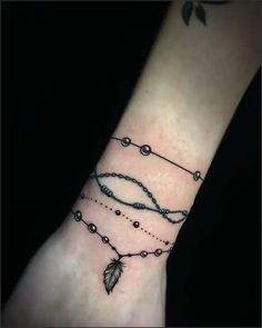 a wrist tattoo with beads and a feather on the left side of the arm,