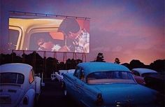 an old car is parked in front of a movie screen with two people on it