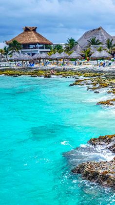 the beach is full of people and thatched umbrellas in the distance, with blue water