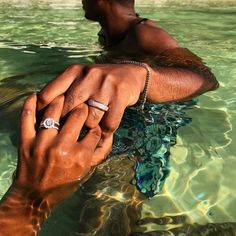 two people holding hands in the water with their wedding rings on top of each other