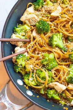 broccoli, chicken and sesame seed noodles in a skillet with chopsticks