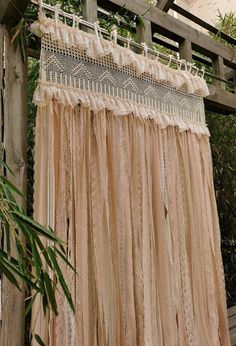 a close up of a curtain hanging from a wooden structure with plants in the background