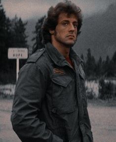 a man standing in front of a street sign with trees and mountains in the background