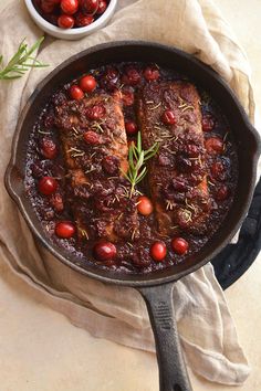 meat with cranberry sauce in a cast iron skillet next to fresh cherries