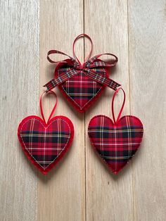 three red plaid heart shaped ornaments hanging on a wooden surface with ribbon and bow around the edges