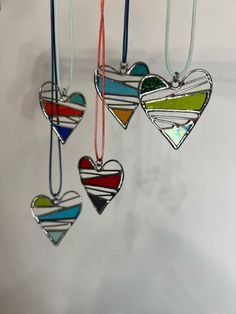 three heart shaped ornaments hanging from strings on a white wall, one is multicolored