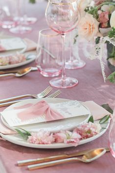 the table is set with pink and white plates, silverware, and napkins