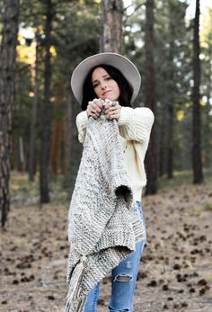 a woman standing in the woods wearing a hat and sweater