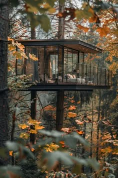 a tree house in the woods surrounded by trees with leaves around it and two people sitting on the deck