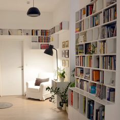 a long narrow room with bookshelves full of books and plants on the wall