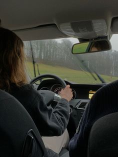 two people sitting in the driver's seat of a car driving down a road