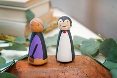 two figurines sitting on top of a wooden table next to leaves and books