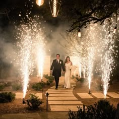 a bride and groom walking down a path with fireworks in the background