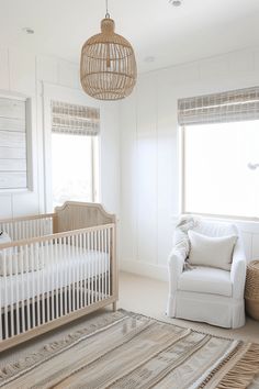 a baby's room with a white crib, chair and large window in the corner