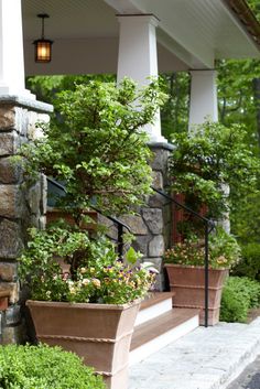 two planters with flowers are on the side of a porch next to a stone wall