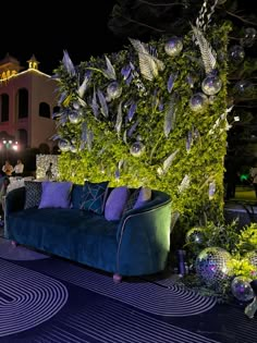 a couch sitting on top of a blue rug next to a green plant covered wall