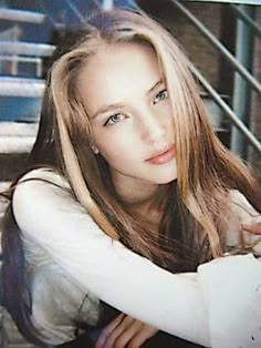 a young woman with long hair posing for a photo in front of stairs and railings