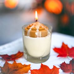 a candle that is sitting in a glass on a table with autumn leaves around it