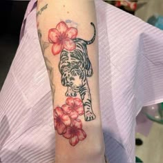 a woman with a tiger tattoo on her arm and flowers around her neck, in front of a white shirt