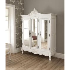 an ornate white armoire with mirrored doors and drawers in a room that has wood floors