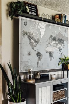 a map is hanging on the wall next to a potted plant and bookshelf