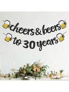 cheers and beers to 30 years banner on a table with flowers in front of it