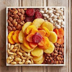 an assortment of nuts and dried fruits in a square tray on a wooden table top