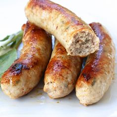 three sausages on a white plate with green beans