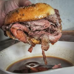 a roast beef sandwich being held over a bowl of soup