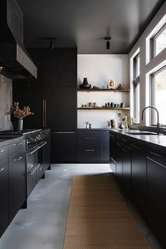 a kitchen with black cabinetry and counter tops next to a large window that looks out onto the outdoors