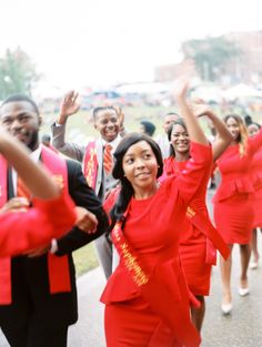 a group of people dressed in red are walking down the street with their arms up