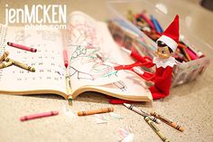 an open book with markers and crayons on the table next to it are two elfs