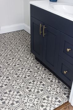 a bathroom with black and white tile flooring, blue vanity cabinetry and sink