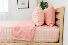 a bed with two pink pillows sitting on it's headboard next to a potted plant