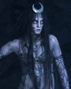 a woman with long hair and tattoos standing in the dark, wearing an elaborate headdress