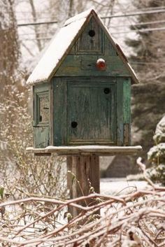 a green birdhouse sitting on top of a wooden post next to trees and snow