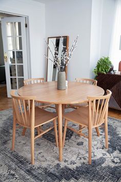 a dining room table with chairs and a vase on it's centerpiece in front of a mirror