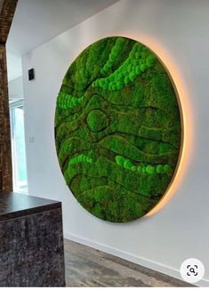 a large green moss covered wall hanging on the side of a white wall next to a wooden table