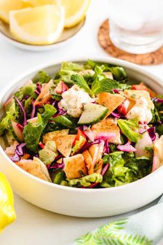 a white bowl filled with salad next to lemon wedges