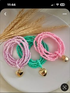 three bracelets with gold bells and beads on a white plate next to some wheat