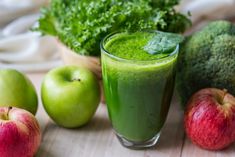 green smoothie in a glass surrounded by apples, broccoli and other vegetables