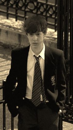 a young man in a suit and tie leaning against a railing with his hands on his hips