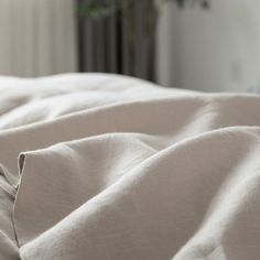 an unmade bed with white linens and a plant in the corner behind it