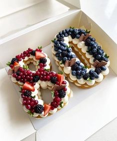 two decorated donuts sitting in a box on top of a white counter with the number 50 made out of fruit