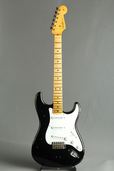 an electric guitar sitting on top of a black stand in front of a gray background