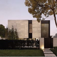 a modern house is shown at dusk with its lights on and trees in the foreground