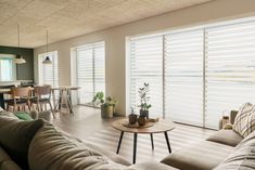 a living room filled with furniture and windows covered in white shutters, next to a kitchen